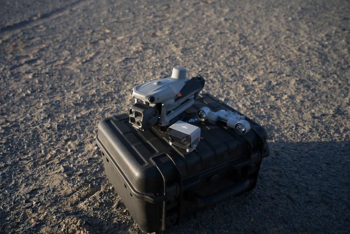 Matrice 4 Series drone and supporting accessories resting on a black transport case on rough ground in late-afternoon light
